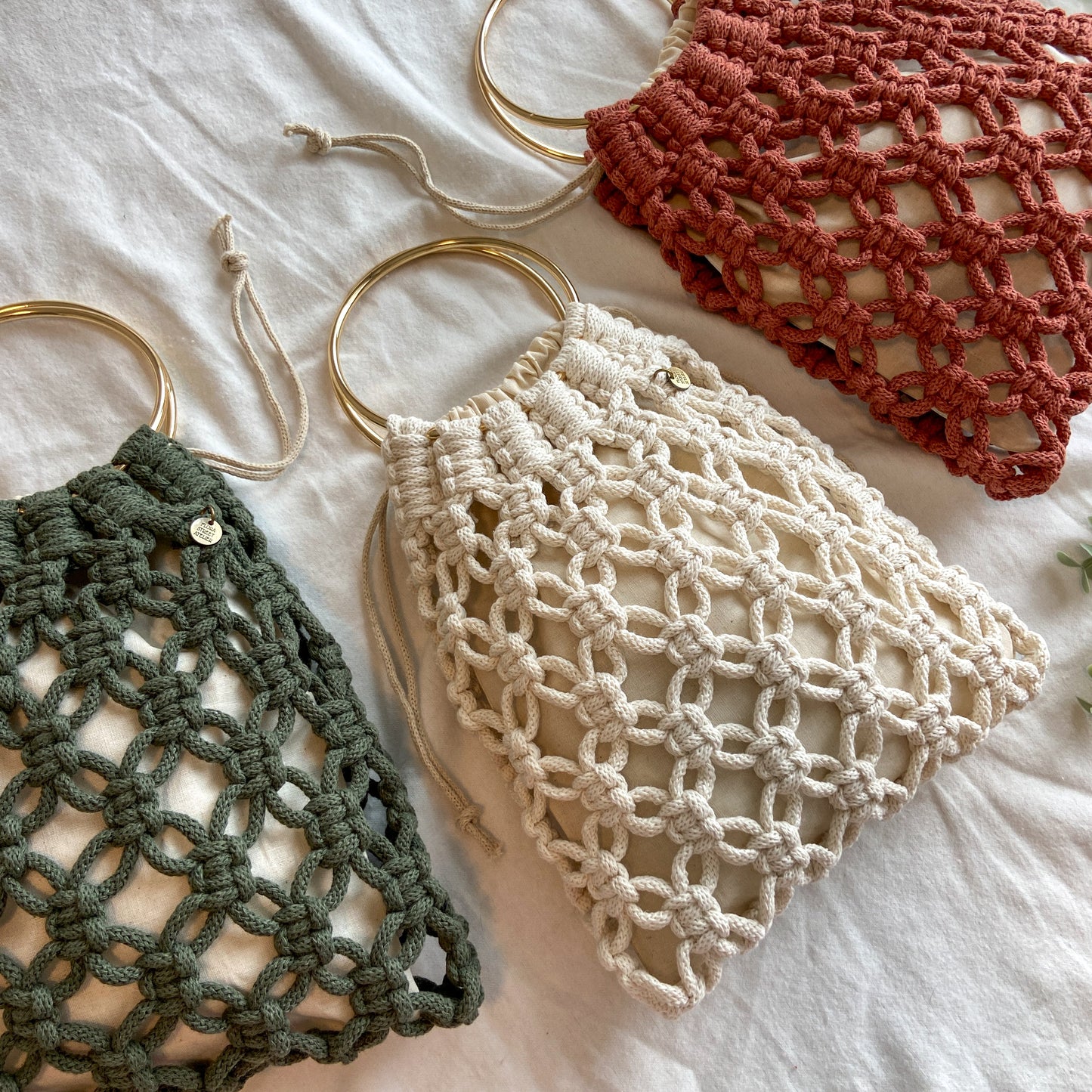 Three macrame bags in green, beige, and red on a light background