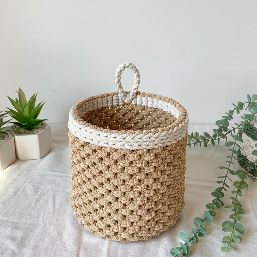 Woven basket with a white rim on a light surface with plants in the background