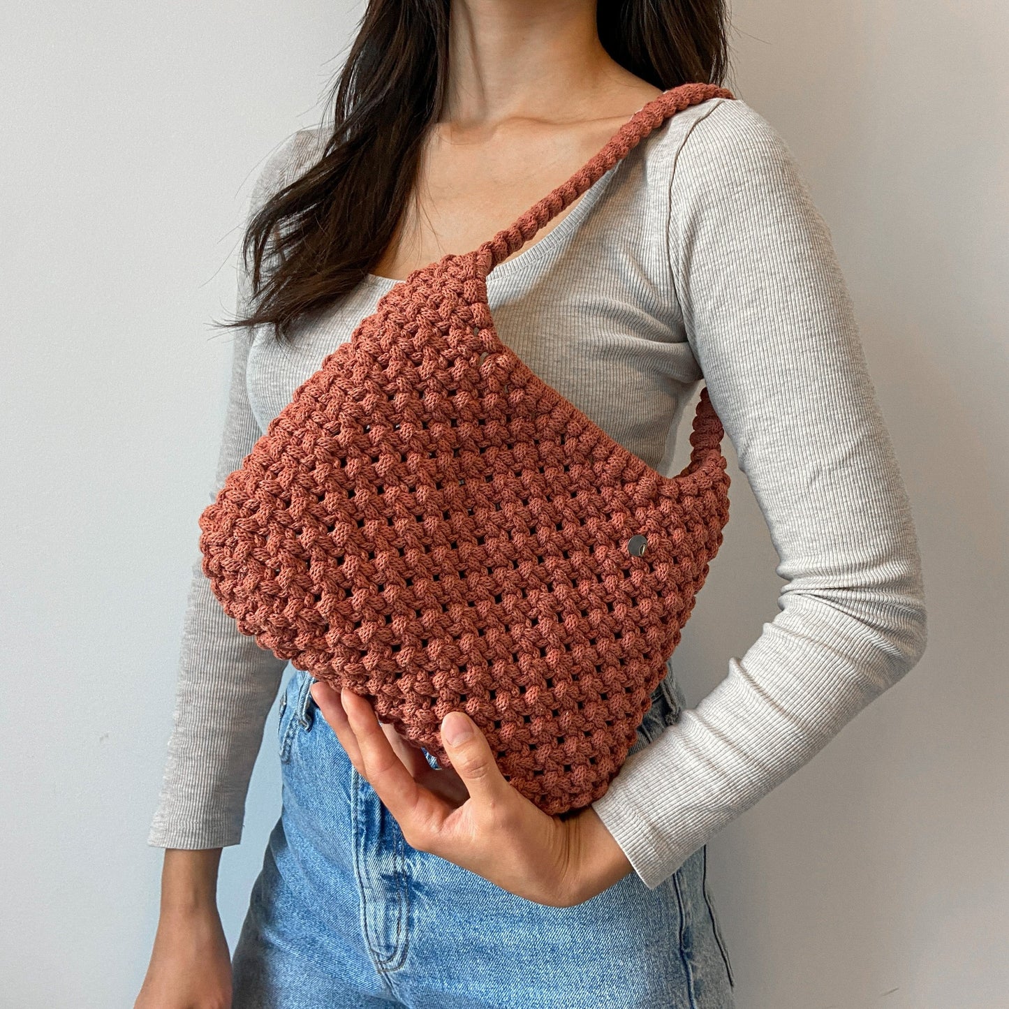 A woman holding a Neutral tone handwoven macrame Hobo shoulder bag with recycled cotton rope and minimalist design
