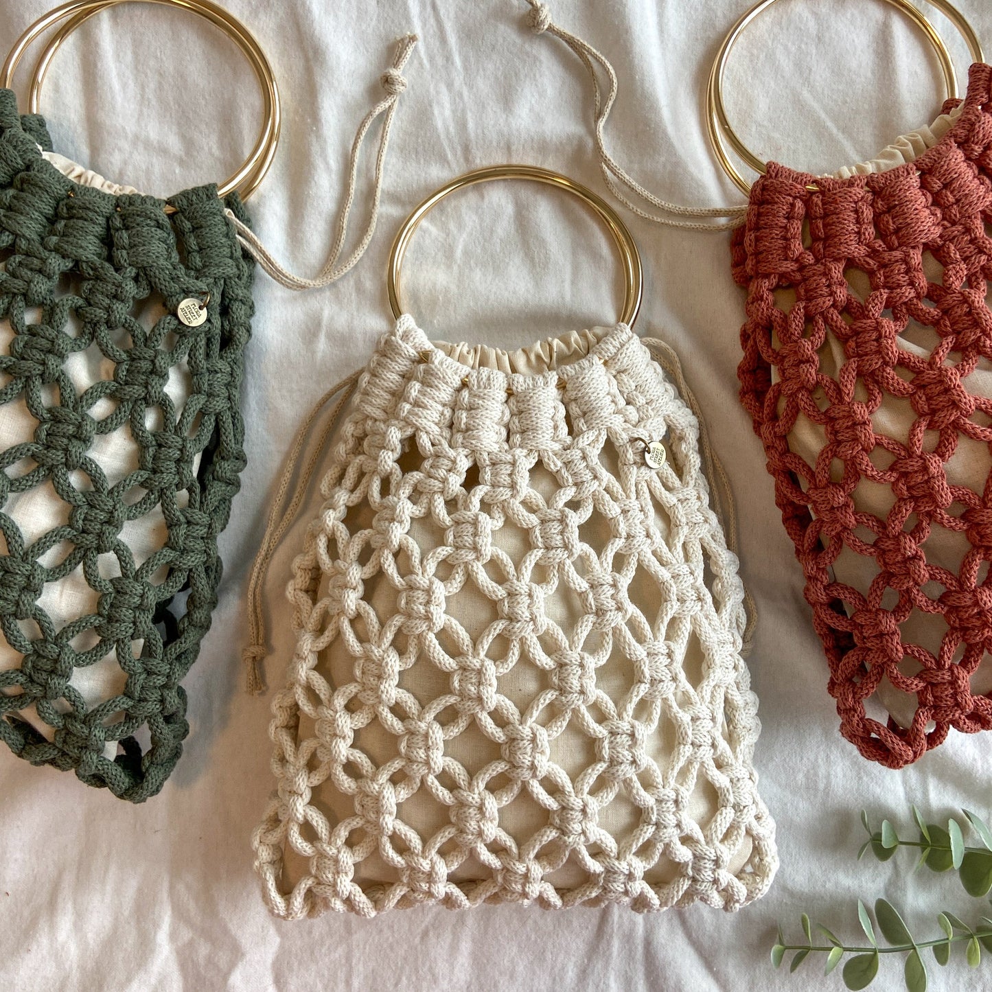 Three macrame net tote bags in green, beige, and red on a light background.
