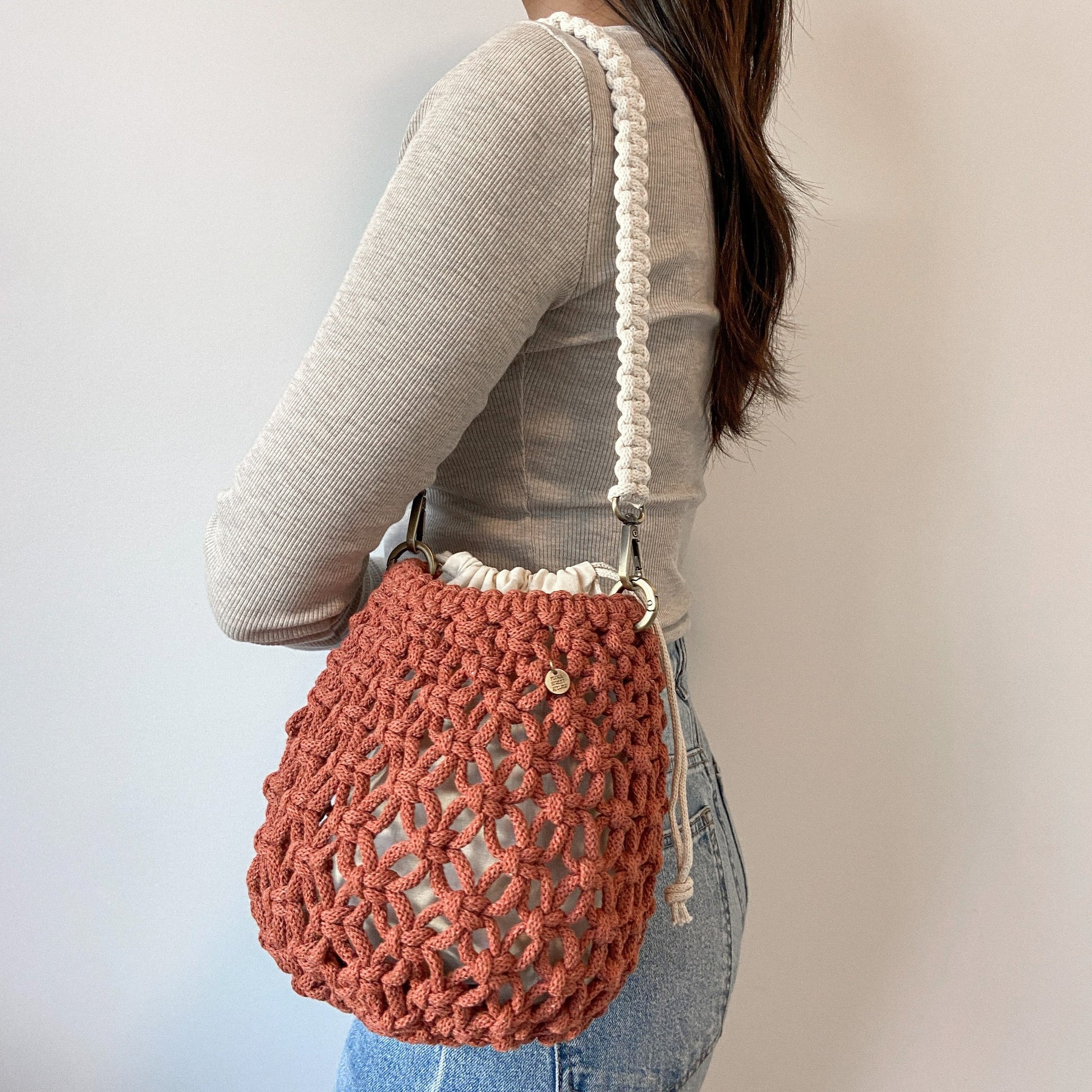 Person wearing a sunset colour woven macrame shoulder bag with a white strap on a plain background