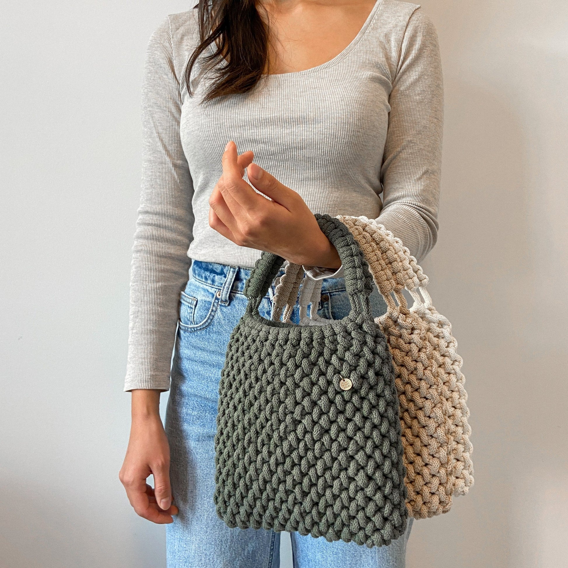 Person holding a knitted Handwoven macrame top handle bag made from sustainable cotton rope, boho accessory
against a plain background