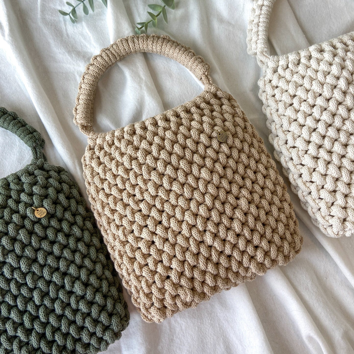 Three knitted macrame top handle handbags made with recycled cotton  in beige, green, and white on a light background