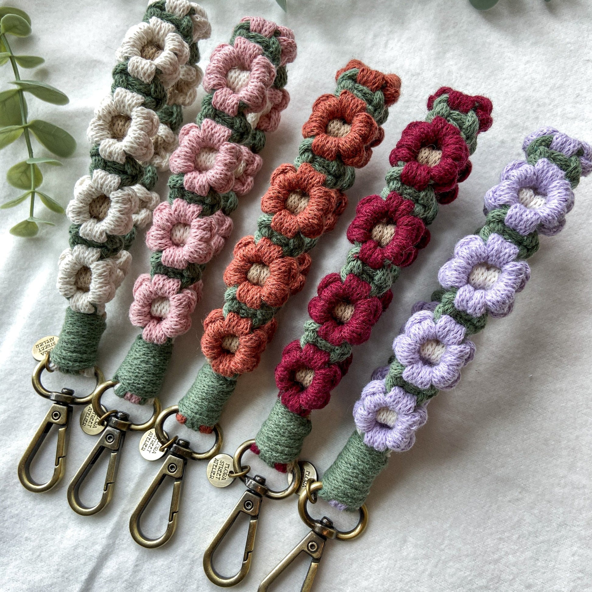 Macrame daisy flower wristlet keychains in white, pink, sunset, burgundy, lavender colour on a white surface