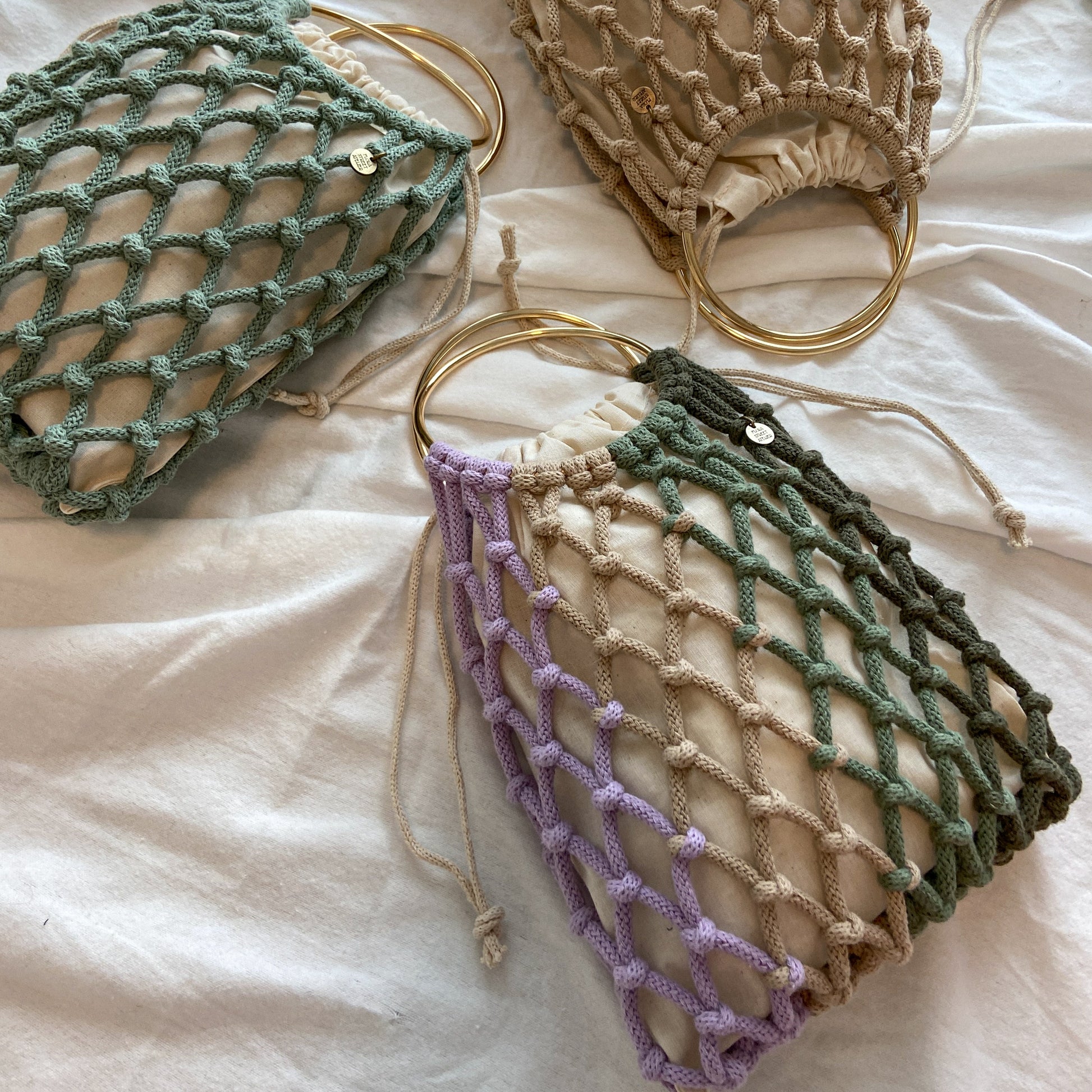 Three mesh macrame bags in green, beige, and purple on a light background