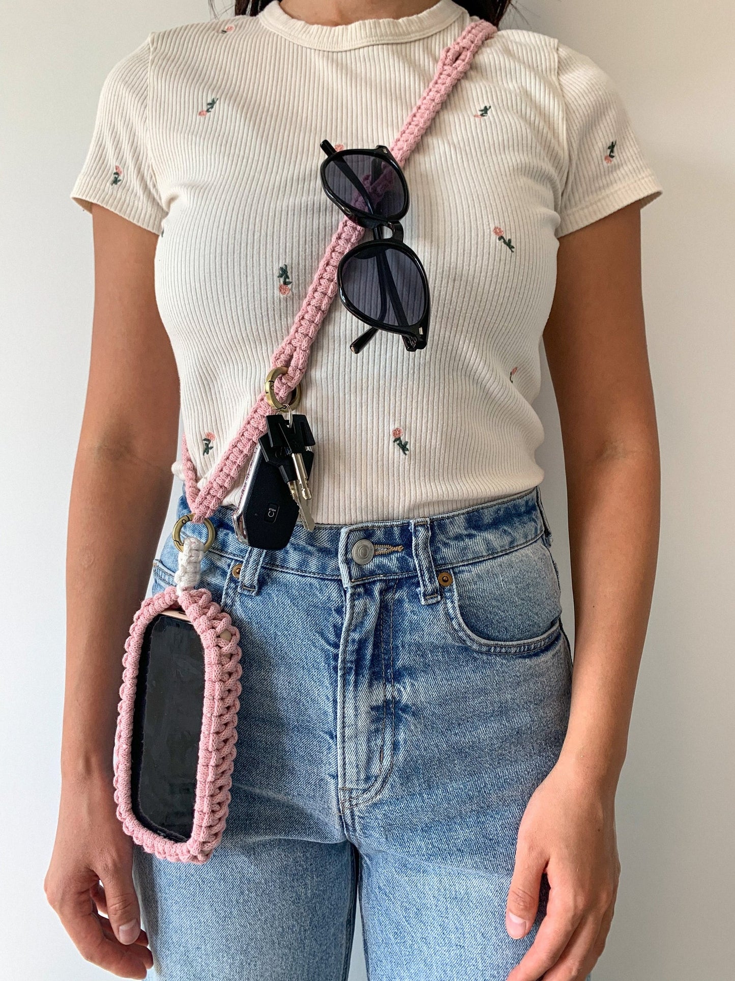 Person wearing a pink crossbody phone holder with sunglasses and keys, standing against a plain background