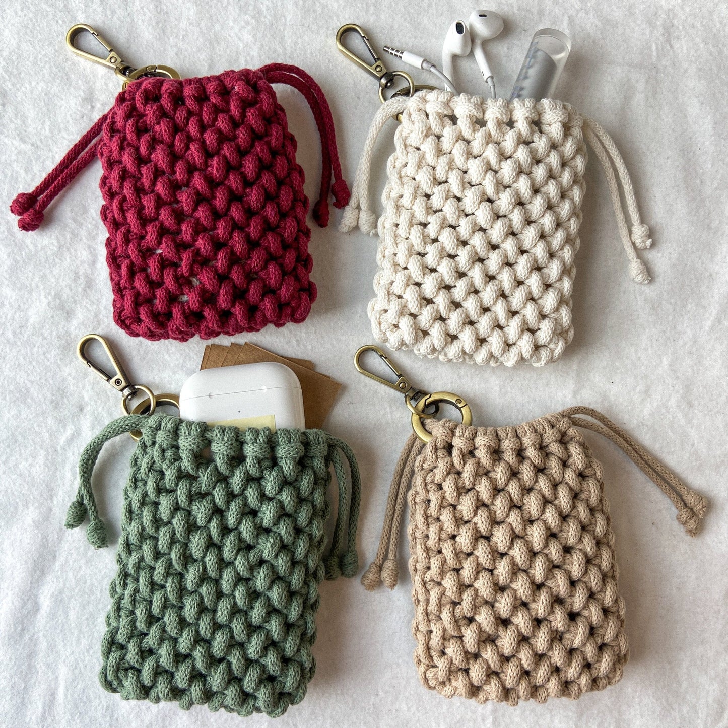 Four hand knotted macrame small pouches with key ring made with recycled cotton cord in red, beige, green, and brown on a light background